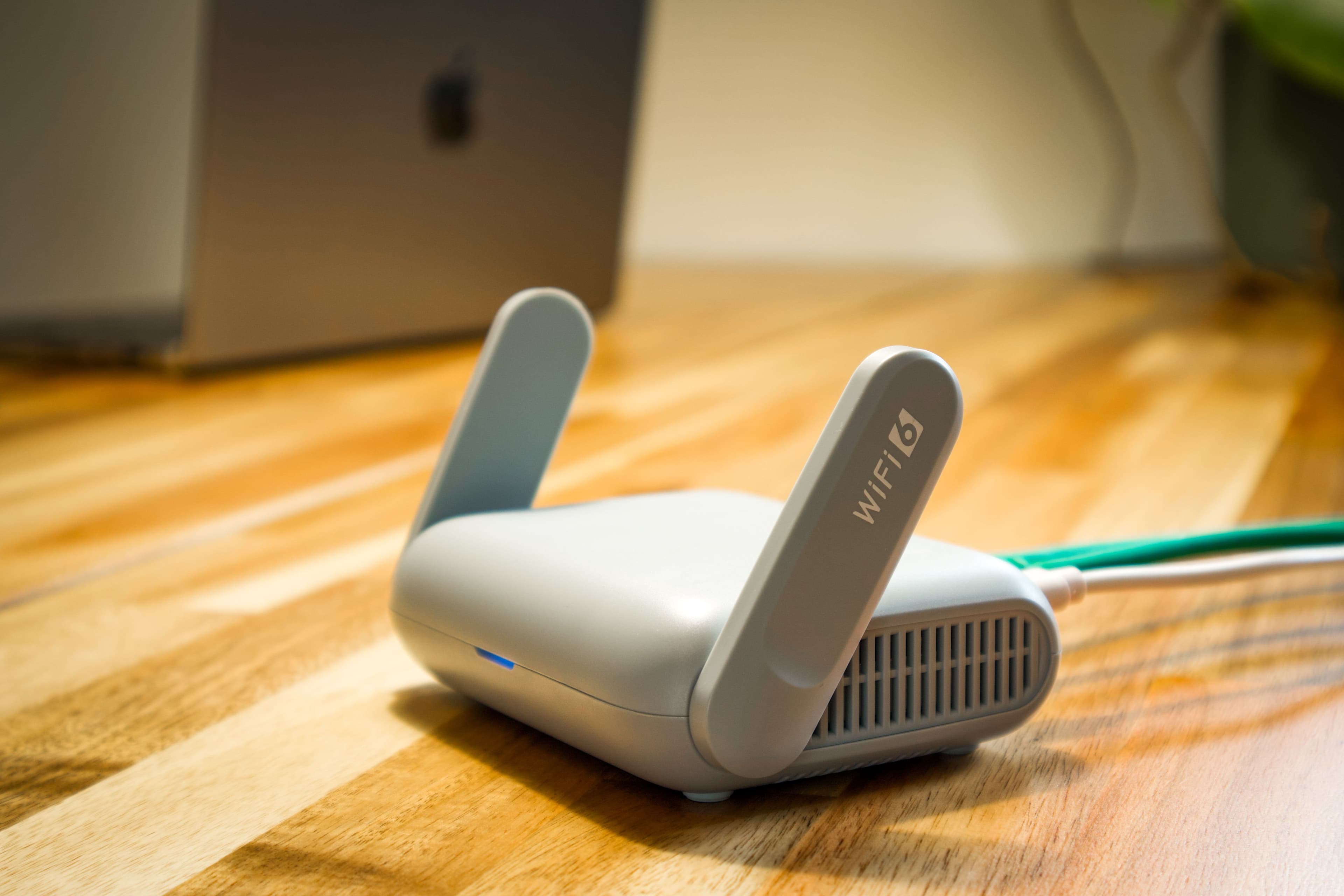 WiFi router on a wooden desk with a laptop blurred in the background.